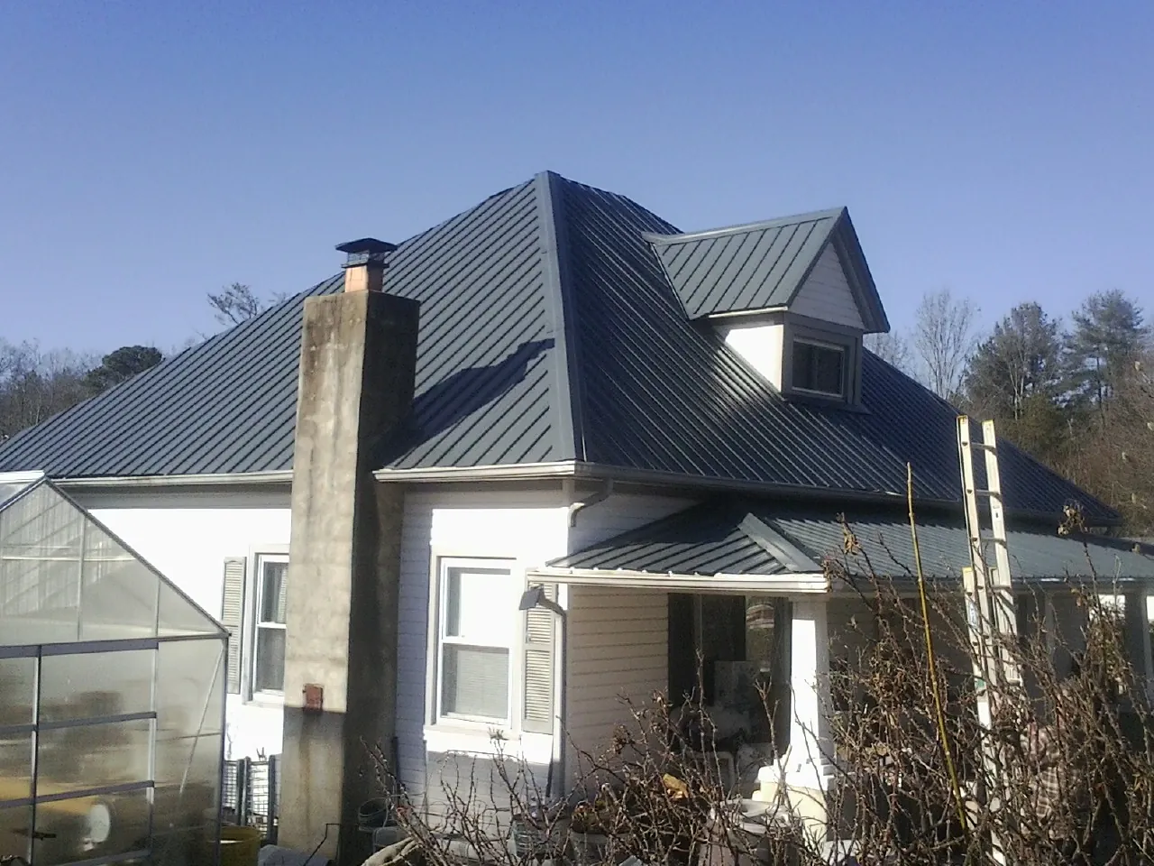 Dark blue standing seam metal roof on a white farmhouse with dormer — Slate & Tile Roof Repair by Roofing Brothers in Greenfield Park