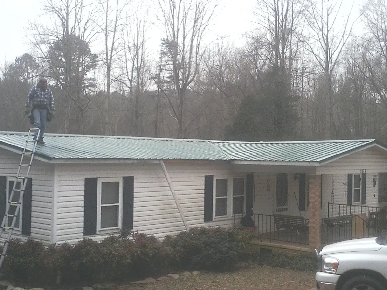 Worker on a ladder beside a new green metal roof on a ranch home in Greenfield Park
