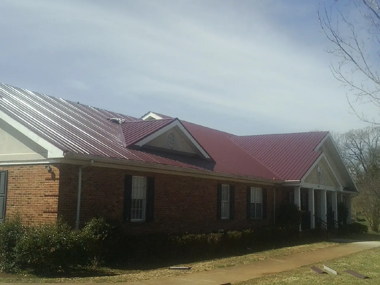 Red metal roof with gabled entries on a long brick building, from a Hail Damage Roof Repair job in Greenfield Park
