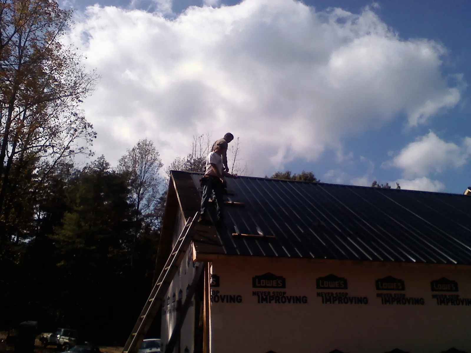 Roofer fastening dark metal panels high against a cloudy sky, from a Roof Inspection job in Greenfield Park