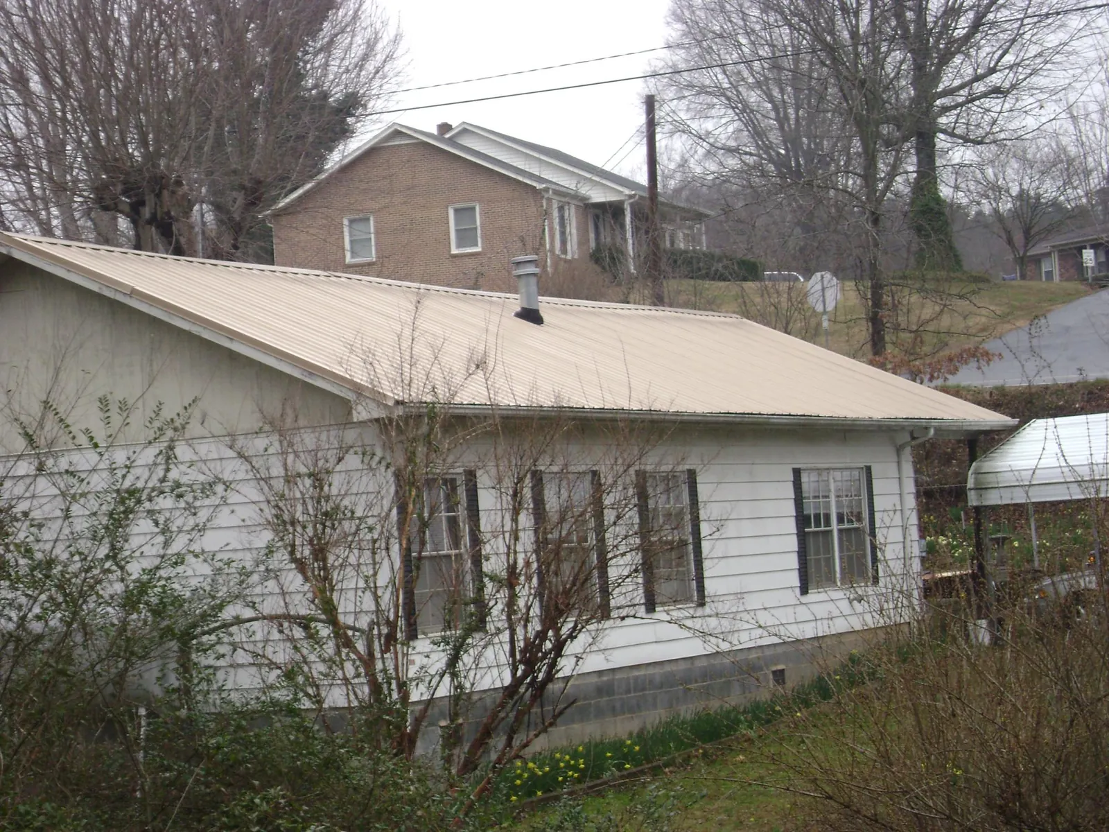 Tan metal roof on a white sided house set into a hillside — Commercial Roofing by Roofing Brothers in Greenfield Park