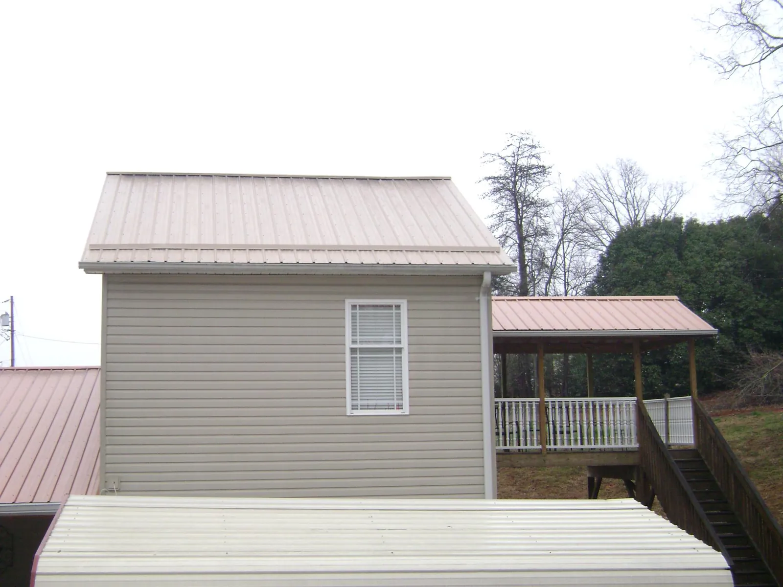 Tan metal roofs on a two story addition and attached porch, from a Roof Replacement job in Greenfield Park